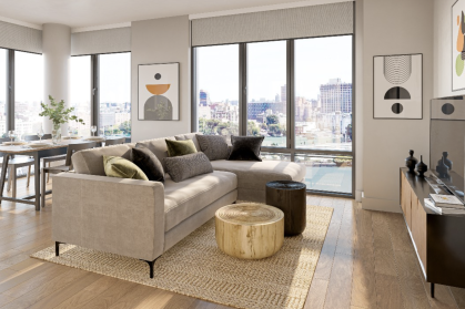 living room with brown sofa, natural colors, wood floors, & large windows overlooking water